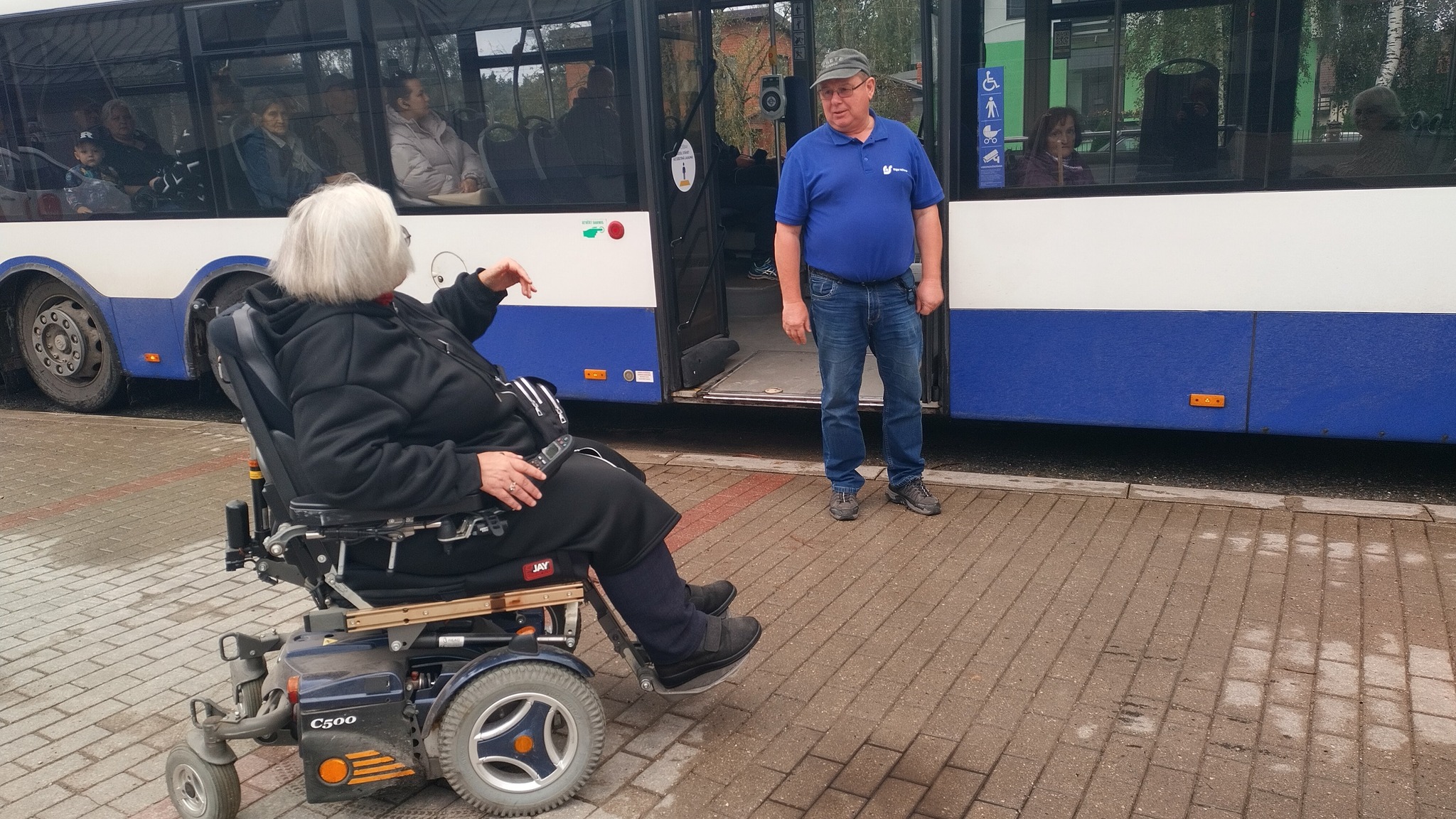 Rita ratiņkrēslā pie autobusa durvīm un šoferis