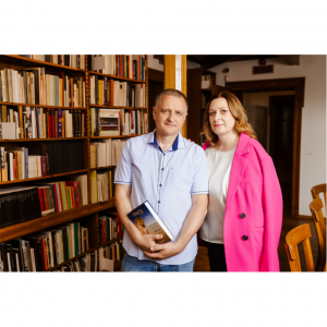 Anatolijs un Inga Baļi stāv bibliotēkā tuvu viens otram.