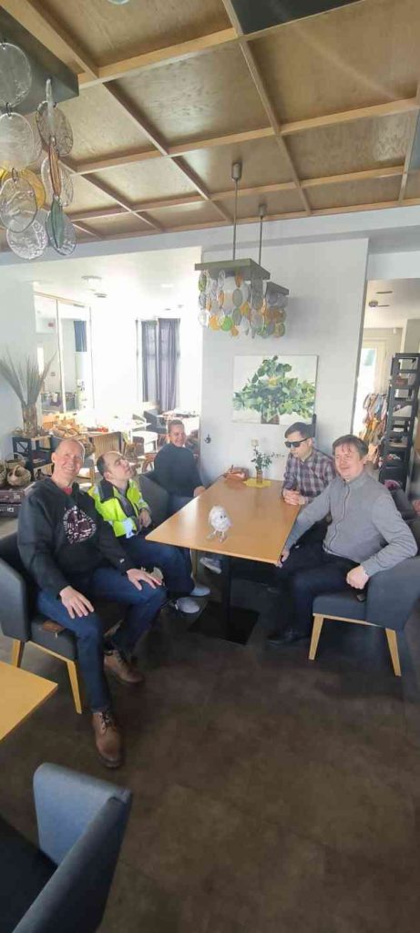 5 cilvēki sēž pie brūnas krāsas galda uz kura ir novietota pūce