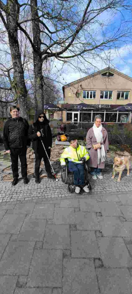 4 cilvēki stāv pie objekta "Ogres lācītis", kurš ir brūnā krāsā un ķepās tur dzeltenas krāsas medus podu