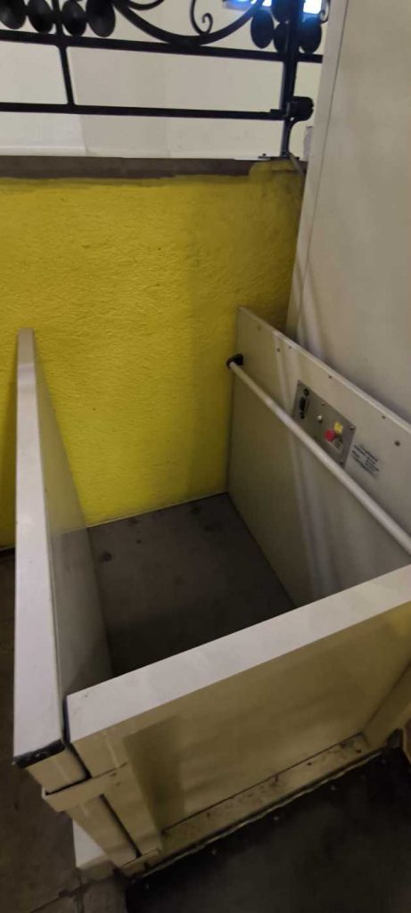 Pelēkas krāsas pacēlājs, aiz tā dzeltenzaļas krāsas siena