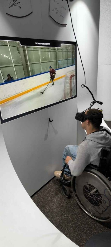 Voldemārs ar VR brillēm pie TV ekrāna spēlē hokeju
