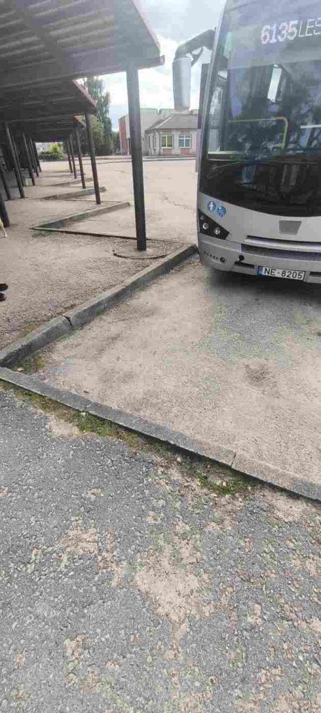 Pelēkas krāsas autobuss piebrauc pie pieturas platformas